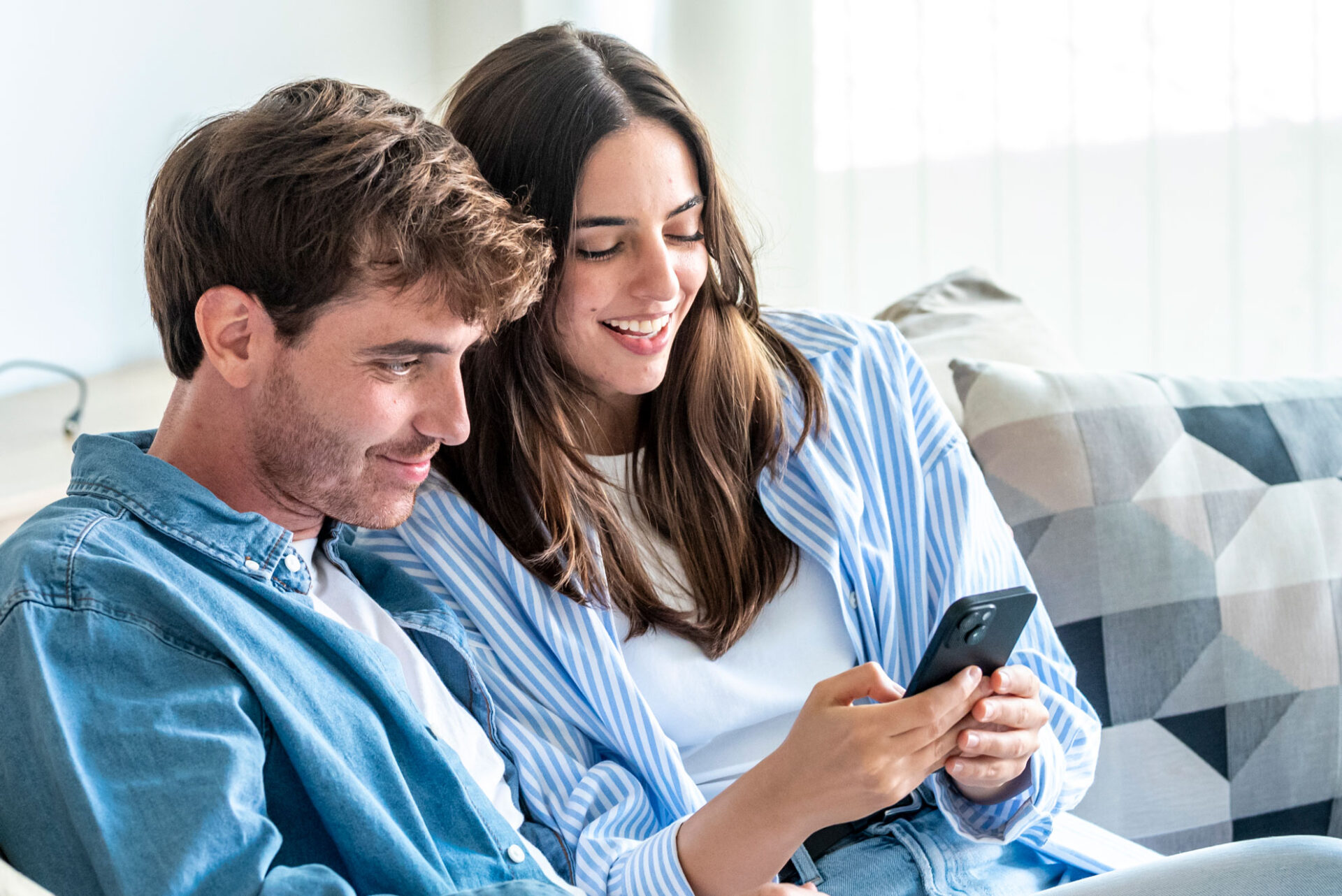 Couple sitting on a sofa browsing free dating apps together on a phone