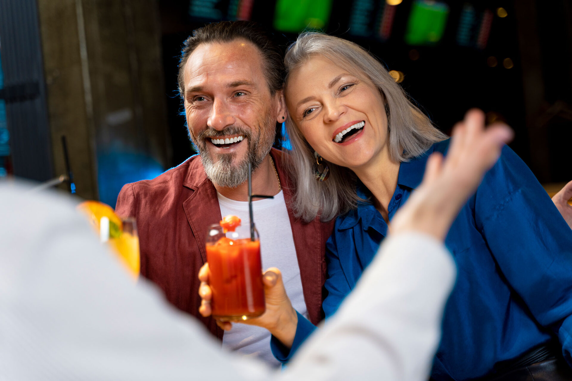 Couple over 50 laughing together with drinks at a bar after meeting on a dating site for over 50s