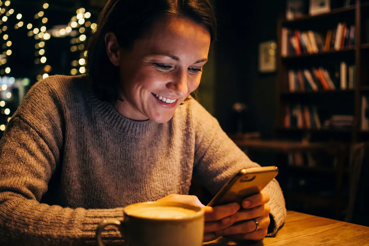 Woman texting on her phone in a cafe, like a member answering a message on Age Gap Dating