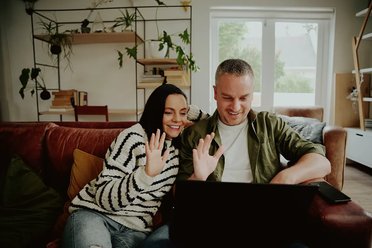 Couple waving at a laptop during a video call, a step Age Gap Dating suggests before meeting