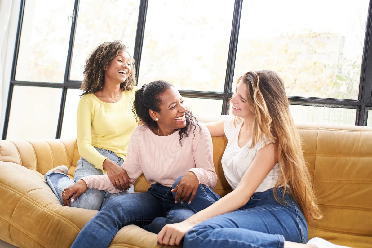 Three friends laughing together on a sofa at home