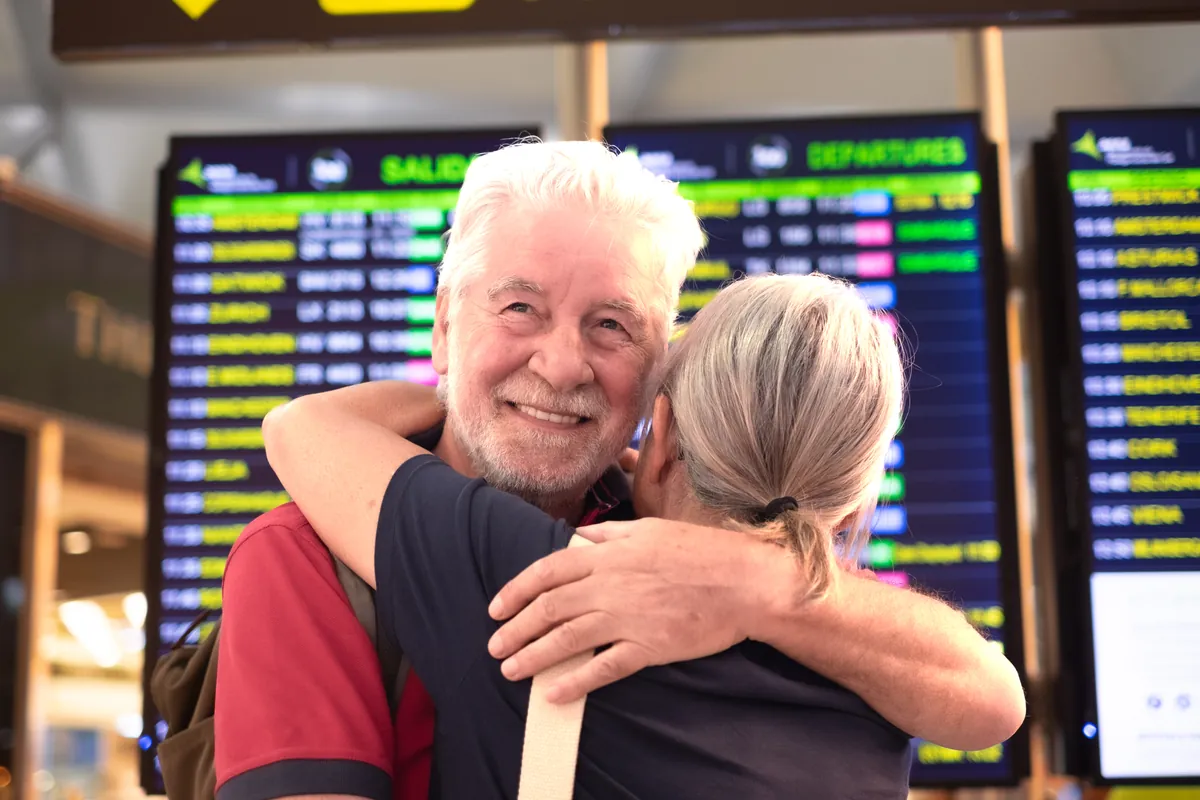 Couple hugging at an airport arrivals board after meeting online