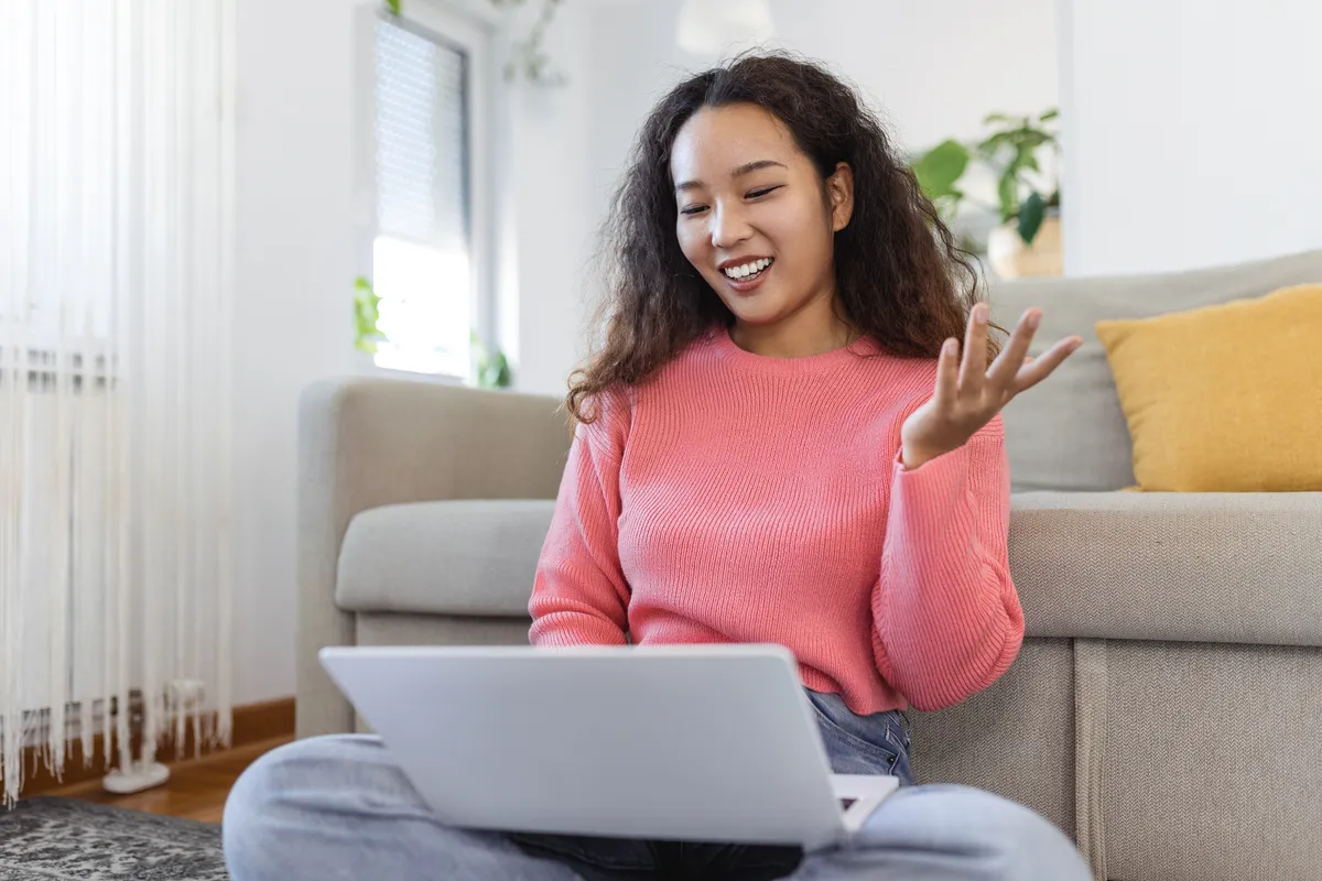 Woman waving at her laptop during a video call before a first date arranged on My Transgender Date