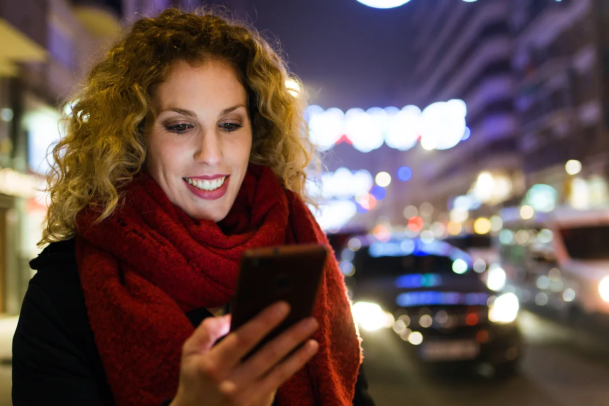 Woman smiling at her phone on a city street at night