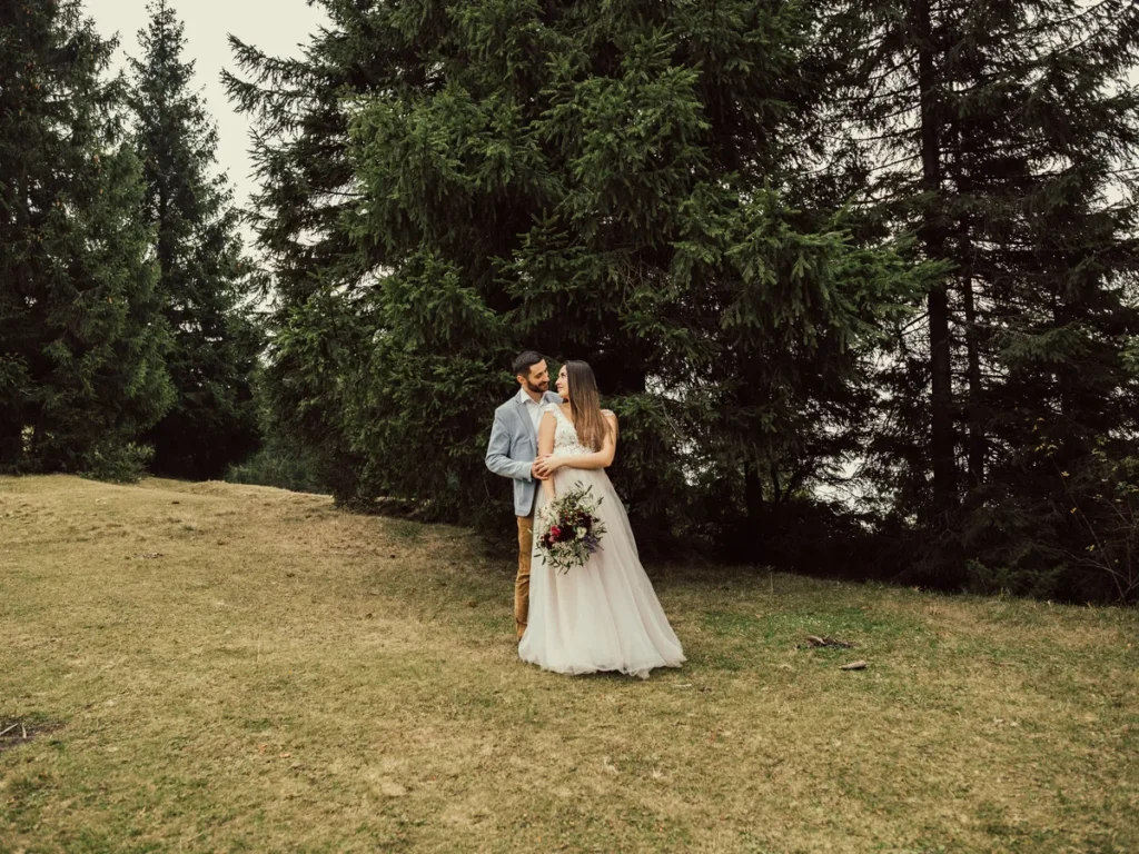 Bride and groom standing in a clearing ringed by evergreen trees