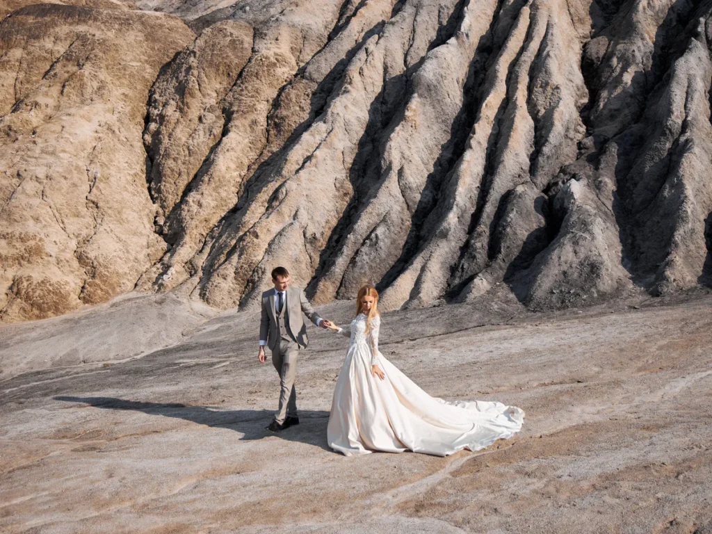 Bride and groom walking on bare rock beneath jagged ridges