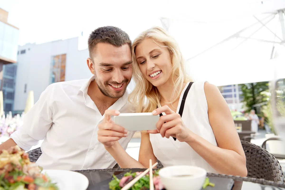 Couple smiling at a dating profile on a phone at a cafe table