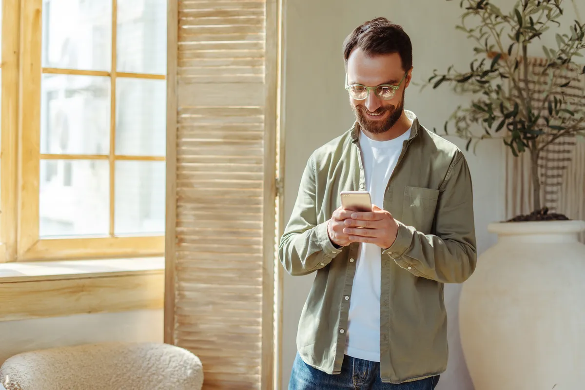 Man in glasses smiling at a new message on his phone at home