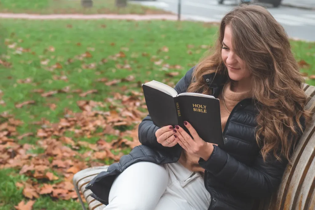 Woman reading a Holy Bible on a park bench in autumn