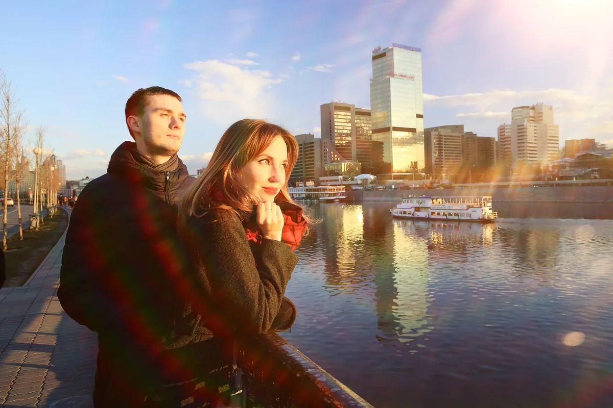 Couple standing by a harbor with city towers lit by the setting sun