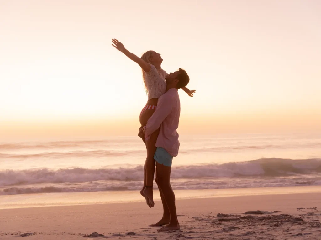 Man lifting his partner on a beach at sunset