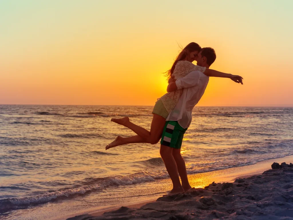 Woman jumping into her partner’s arms on a beach at sunset