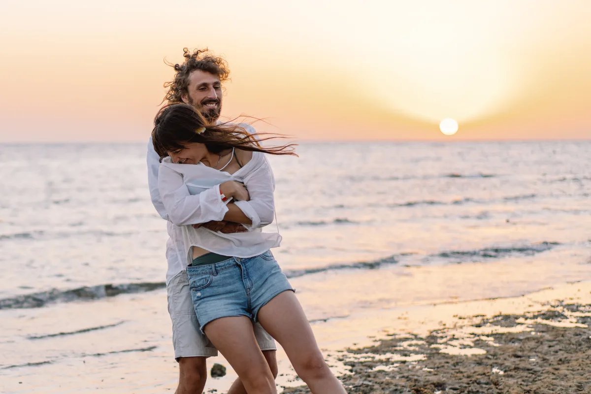 Couple hugging and laughing on a beach at sunset