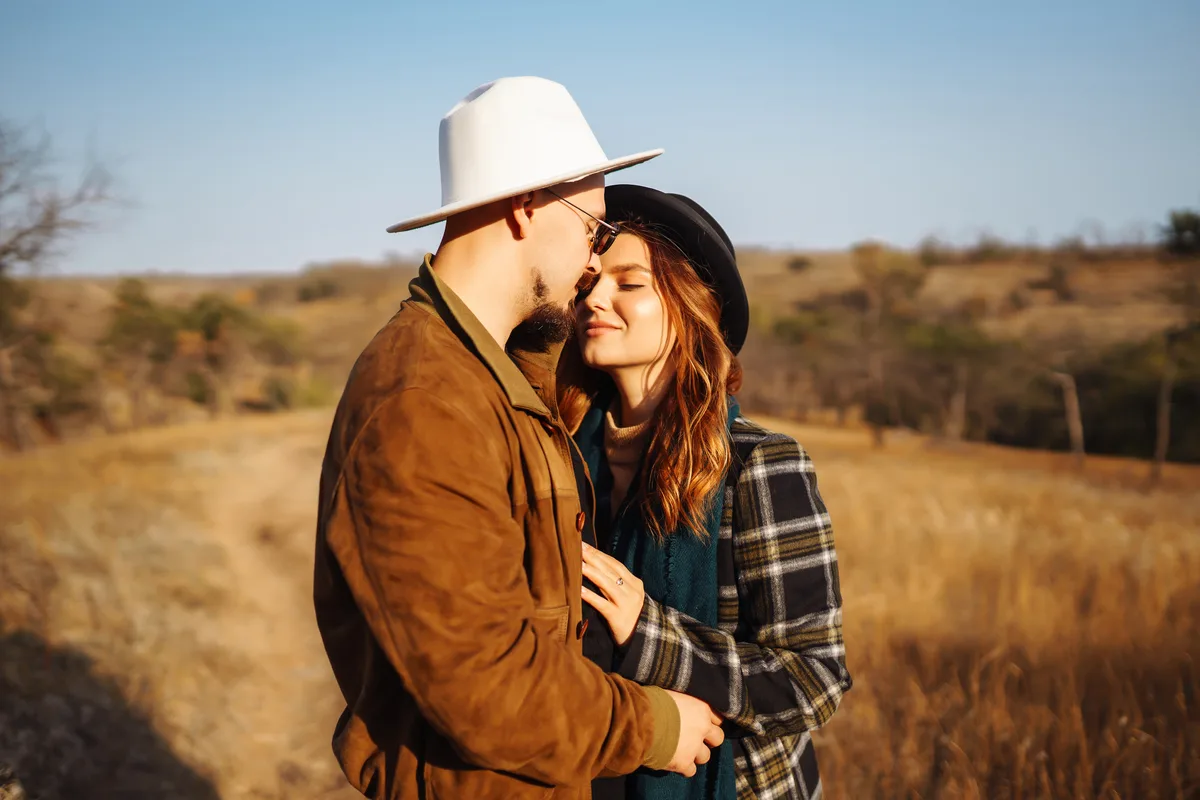 Couple in cowboy hats embracing in an open grassland