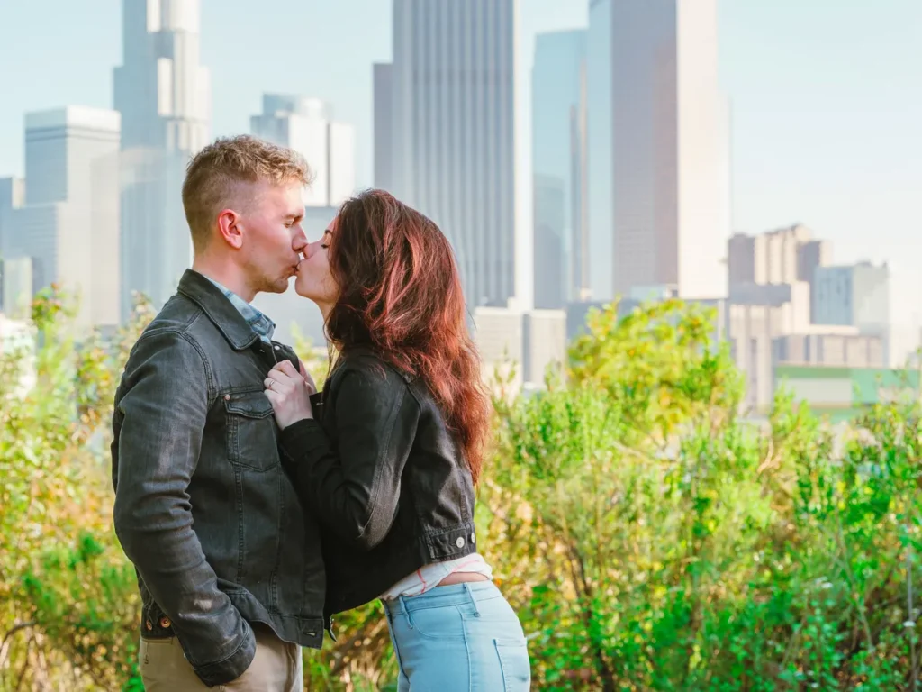 Couple kissing in a park with a city skyline behind them