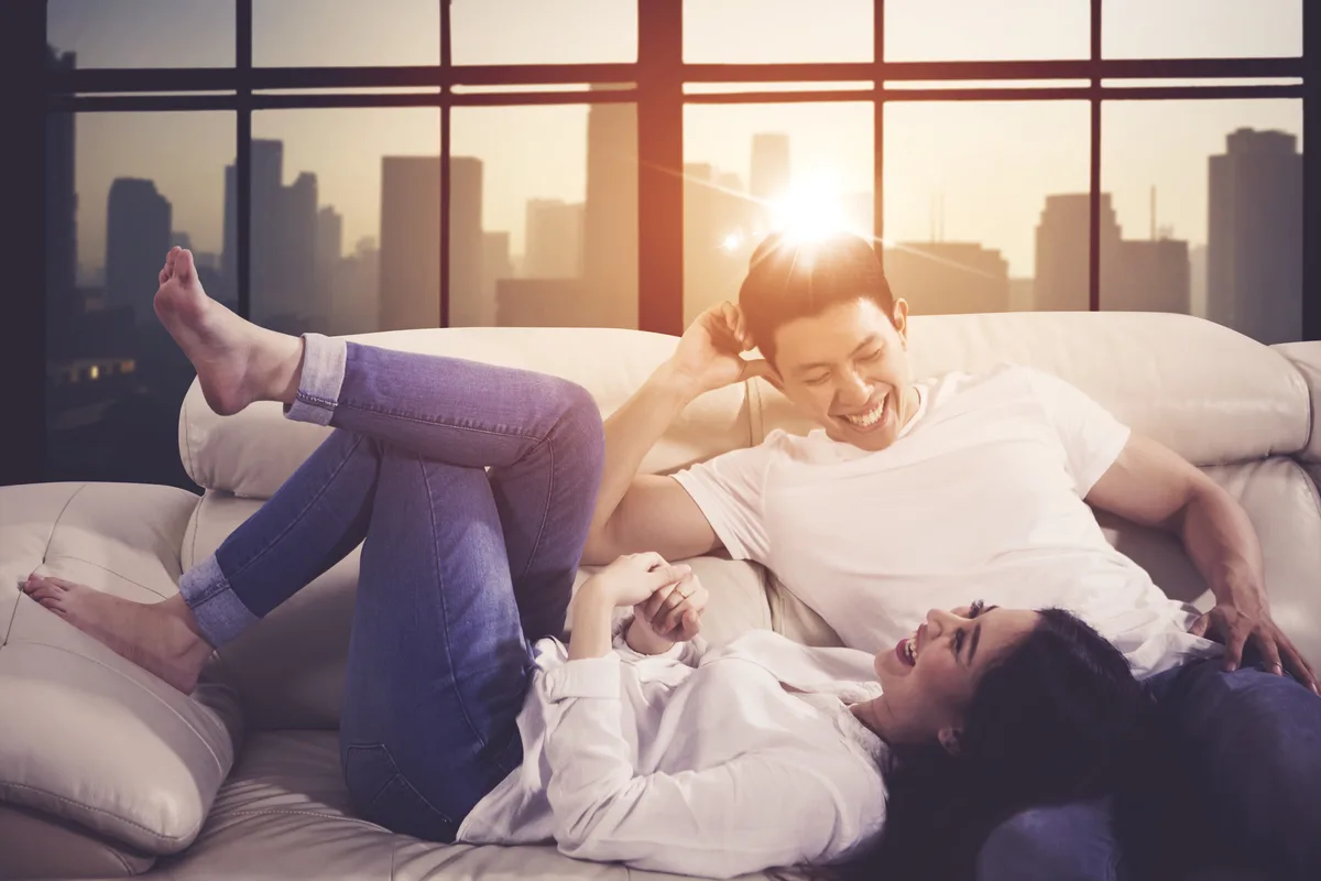 Couple laughing on a sofa in an apartment with a city view