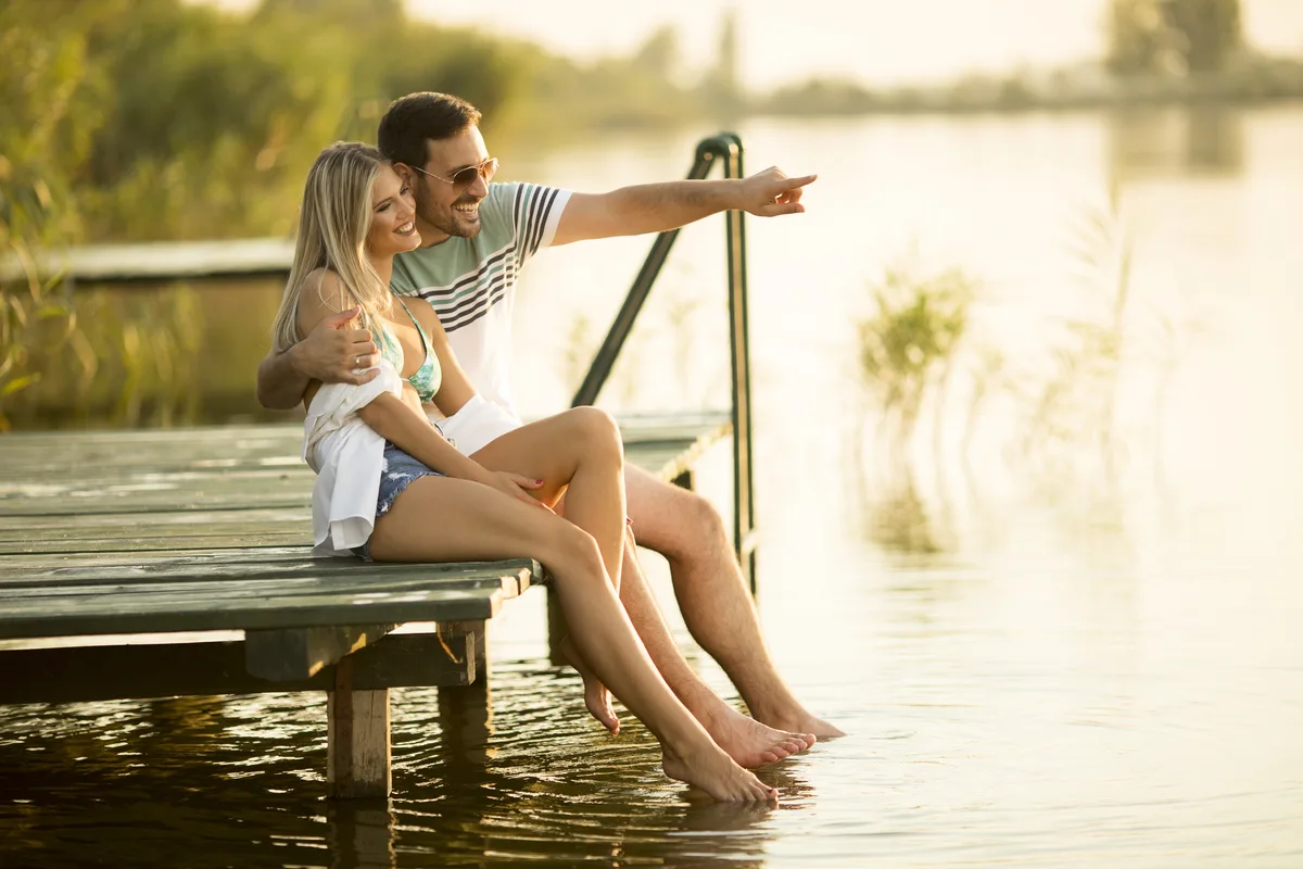 Couple sitting on a wooden pier with their feet in the lake