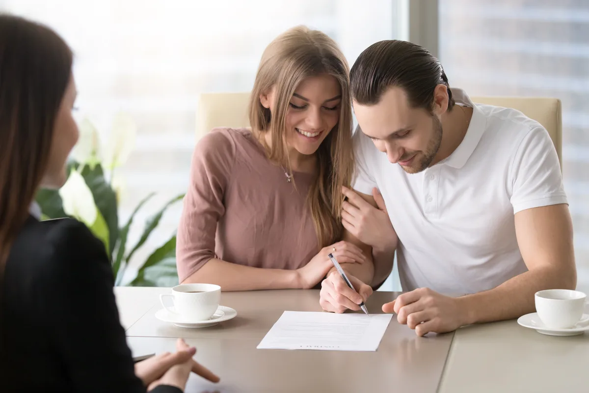 Couple signing a written agreement at a table with an advisor