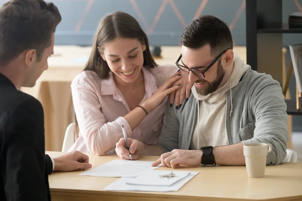 Couple signing an agreement as an agent looks on