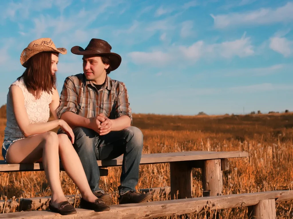 Couple in cowboy hats sitting on a wooden bench in open country
