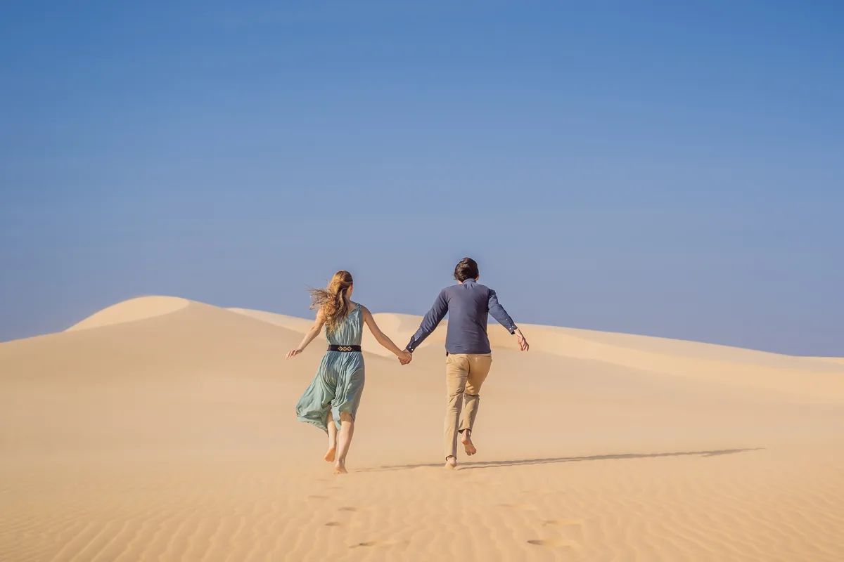 Couple walking hand in hand across sand dunes