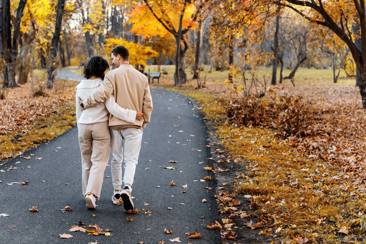 Couple walking arm in arm along an autumn park path