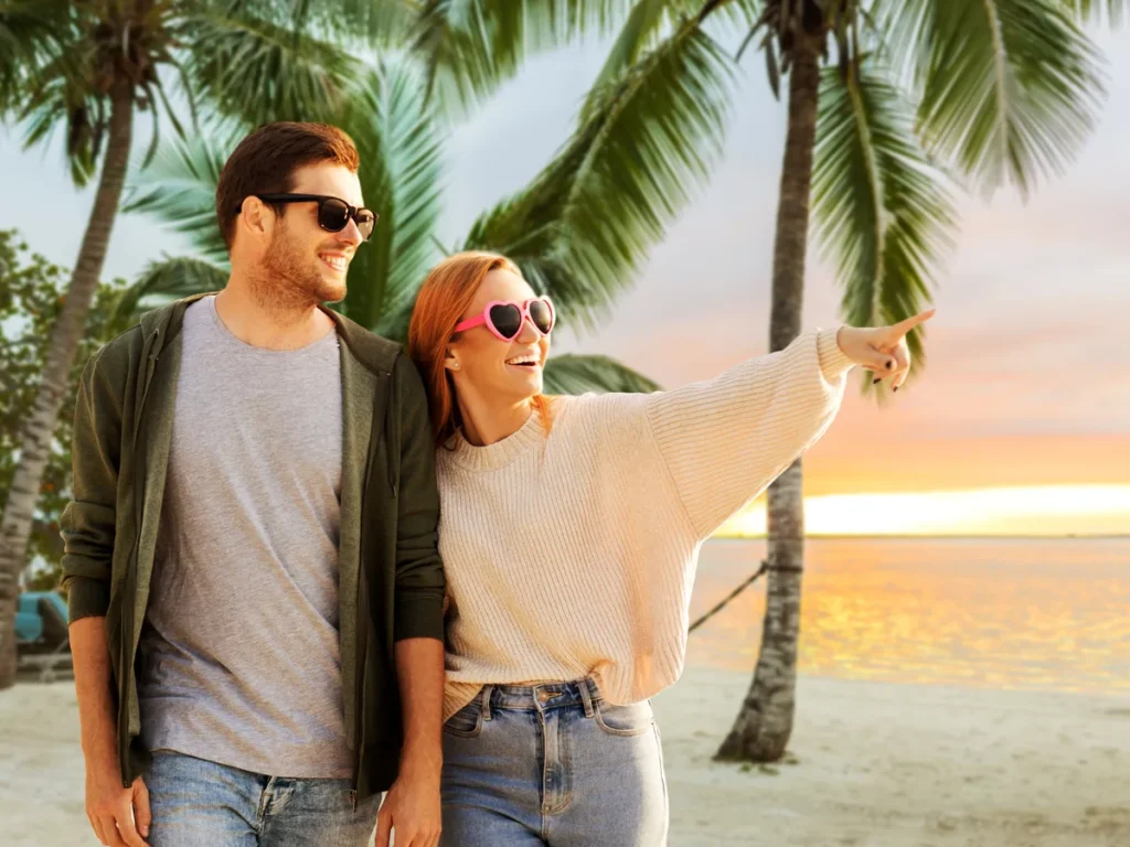 Couple walking on a beach lined with palm trees at sunset