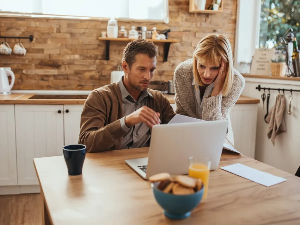 Couple looking at a laptop at the kitchen table over breakfast