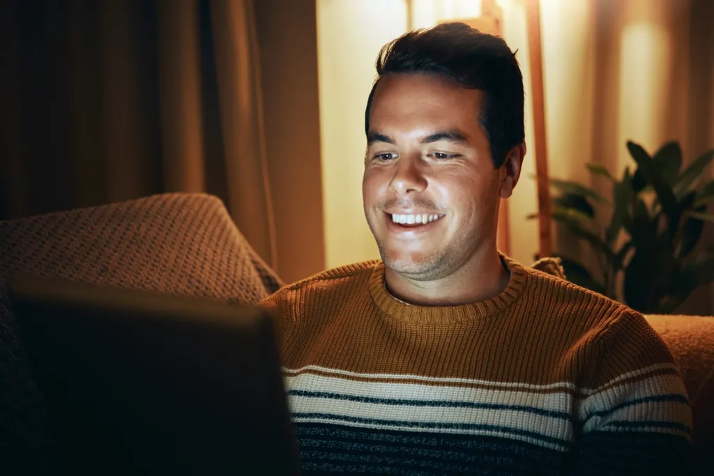 Man smiling at his laptop during an evening video chat at home