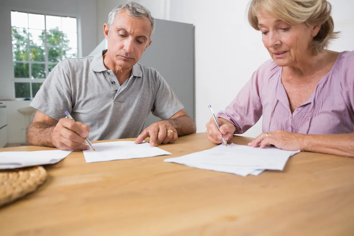 Older couple signing papers together at a kitchen table