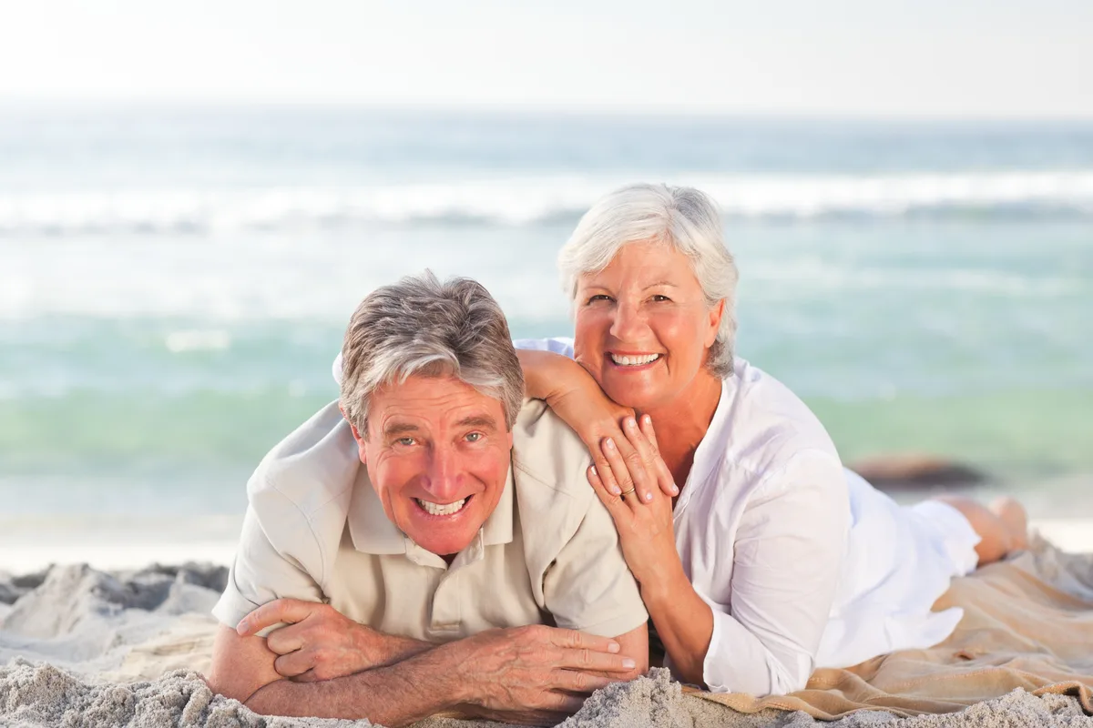 Smiling older couple lying together on a sandy beach