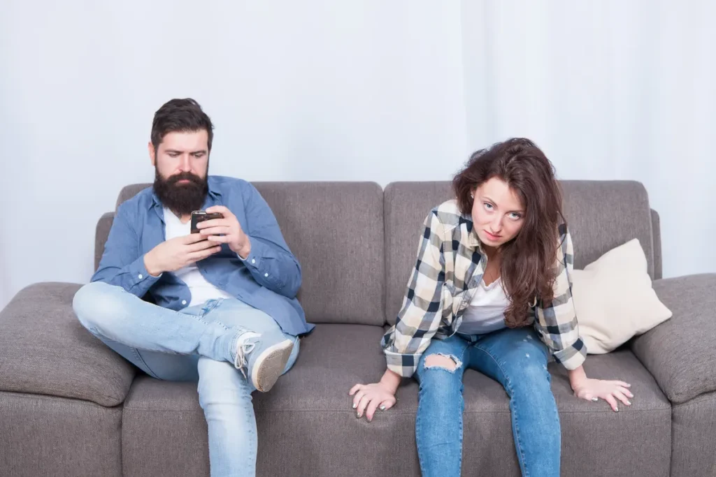 Woman leaning toward her partner while he looks at his phone on the sofa