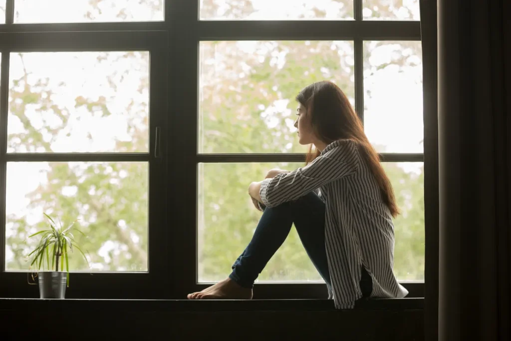 Woman sitting alone on a window ledge, looking outside