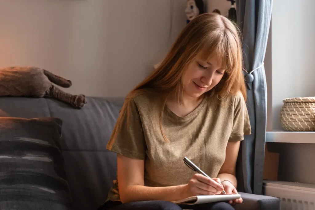 Woman writing in a notebook while sitting on her sofa